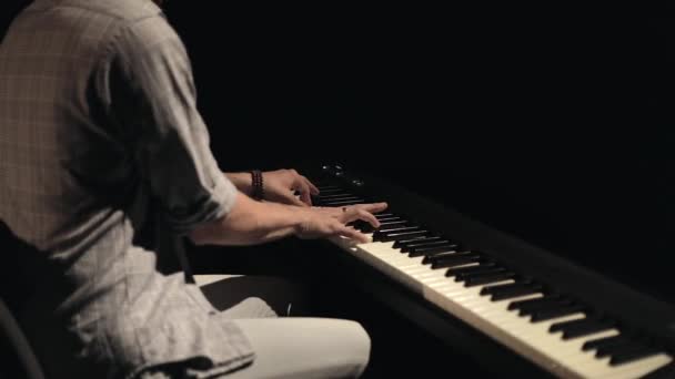 Mãos de um jovem bonito que gosta de tocar piano eletrônico em um quarto escuro à noite, tiro estático. Close-up — Vídeo de Stock