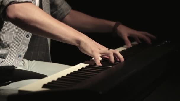 Handen van een knappe jongeman die 's nachts graag elektronische piano speelt in een donkere kamer, statische opname. Close-up — Stockvideo