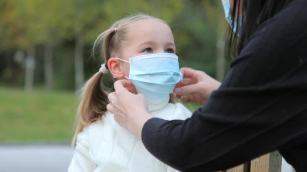 Una giovane madre caucasica si mette una maschera protettiva per sua figlia. La ragazza guarda sua madre e sorride. primo piano rallentatore. — Video Stock