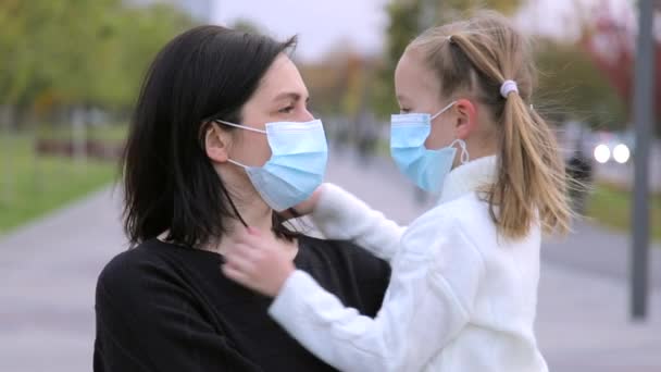 Ritratto di una giovane donna caucasica premurosa con una maschera medica protettiva, che guarda attentamente sua figlia. Una ragazza indossa una maschera medica per sua madre durante una pandemia al rallentatore. Sfocato — Video Stock