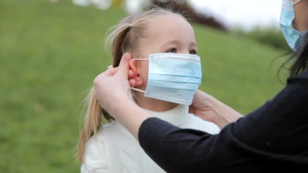 Una giovane madre caucasica si mette una maschera protettiva per sua figlia. La ragazza guarda sua madre e sorride. primo piano rallentatore. — Video Stock