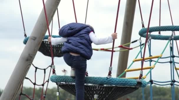 Uma garotinha desce uma escada de corda em um playground infantil inovador. Ela foi capaz de fazê-lo sozinha e ela está muito feliz. Negrito independente caucasiano criança menina. — Vídeo de Stock