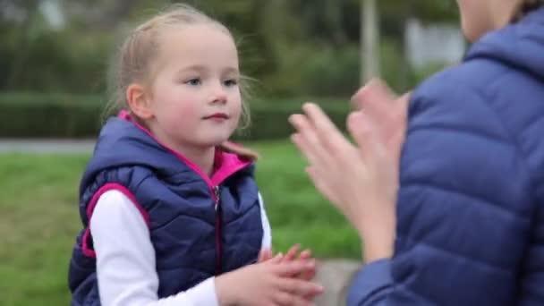 Happy Caucasian child girl in casual clothes plays with her sister clapping her hands in the afternoon on the childrens playground. They have fun together, laugh, enjoy the weekend outside. — стоковое видео