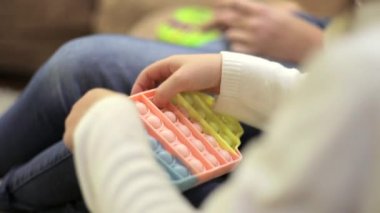 Popüler bir silikon anti-stres pop-it oyuncağını oynayan bir kızın ellerine yakın çekim. Anaokulu öğrencisi de baloncuklara basarak basit dokunmatik hareketler yapıyor.. 