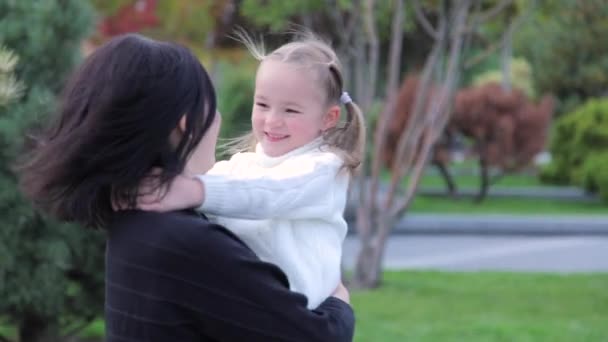 A happy young European mother holds a cute, funny baby girl in her arms and circles around. They laugh and have a good time on Mothers Day. Mom and little daughter have fun together in the city park — Vídeo de Stock