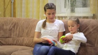 Çocuklar odadaki kanepede oturmuş popüler bir masa oyunu oynuyorlar. Birbirlerine silikon, basit gamzeler ve pop-it oyuncakları takıyorlar. Mavi kot pantolon ve beyaz tişörtle. Orta boy..