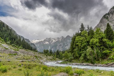 Koyu bulutlar ve nehir aşağı yeşil vadi manzaralı.