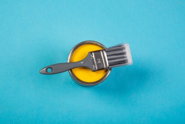 New brush and metal can of paint on blue table top view. Pastel color. Closeup. Preparation for repair work of home. Empty place for your text.