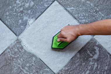 İnsan elinin üst görüntüsü yeşil renkli plastik bir zemin temizleyicisi ile yerleri fırçalamak için kullanılır..