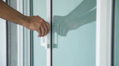 Cam kapıyı açan bir adamın elinin yakın çekimi..