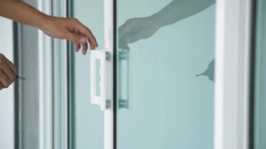 Bir adamın elinin yakın plan çekimi. Bir anahtarla cam kapıyı açıyor..