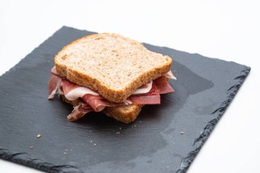 Beyaz arka planda çiğ jambonlu ve salatalı ekmekli sandviç.