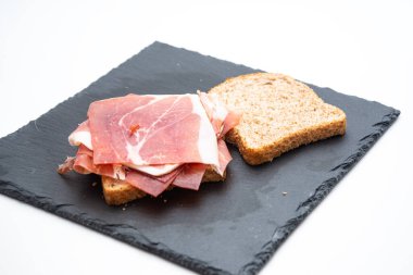 Beyaz arka planda çiğ jambonlu ve salatalı ekmekli sandviç.