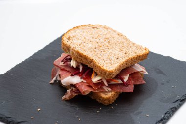 Beyaz arka planda çiğ jambonlu ve salatalı ekmekli sandviç.