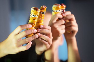 Çocukların elleri, hamur ve sosisten yapılmış mumya şekilli Cadılar Bayramı atıştırmalıklarını tutuyor.