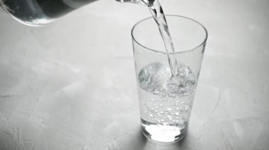 Su, gri arka plandaki bir bardağa dökülüyor.