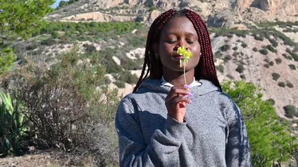 Chica negra sostiene y respira el aroma de una flor — Vídeos de Stock