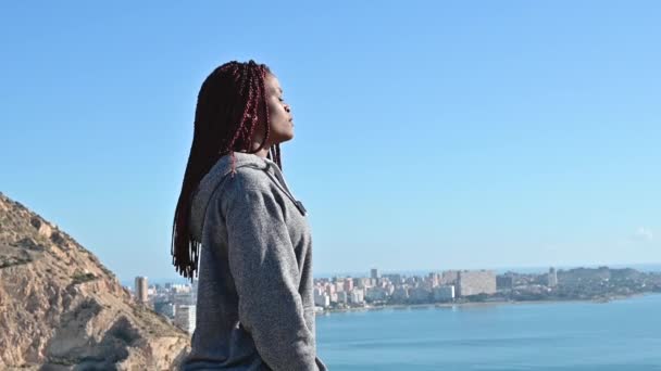 Mujer negra de pie sobre el cielo y el mar y respirando — Vídeos de Stock