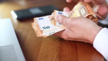 Avro banknotlarını sayan adam masada oturuyor.