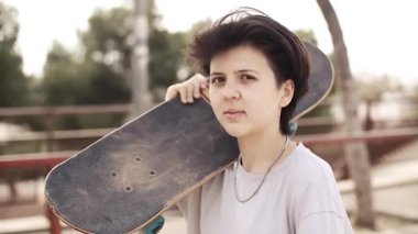 Genç kız omuz kaykayını tutuyor ve kaykaya biniyor.