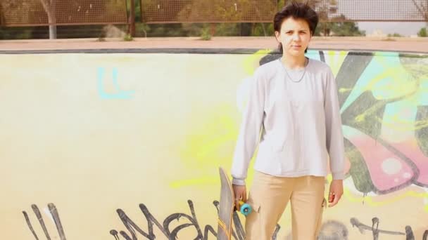Adolescente sosteniendo monopatín en un skatepark — Vídeo de stock