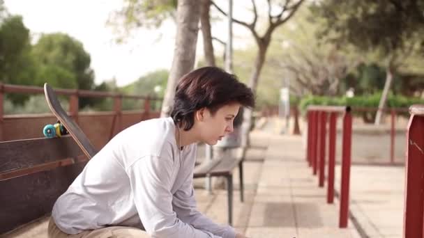 Грустная девочка-подросток сидит на стуле в скейтпарке — стоковое видео