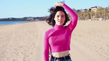 Genç bir kadın kıyı şeridinde yürüyor ve gülüyor