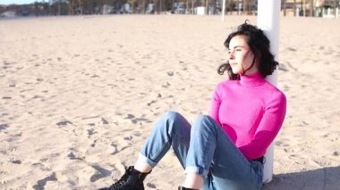 Genç kadın kumsalda oturuyor ve gülümsüyor.