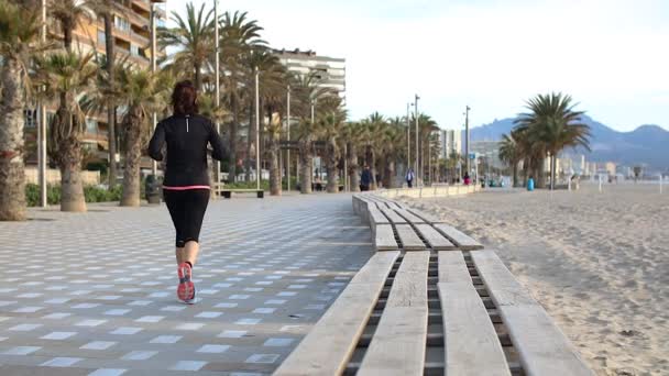Spor kıyafetli bir kadın plajda koşuyor. — Stok video