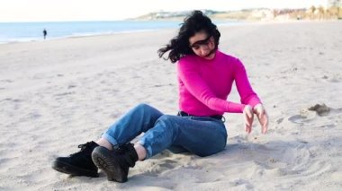 Genç bir kadın ellerinden kum fırlatıyor, ağır çekimde.