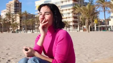 Genç bir kadın sahilde sigara içiyor.