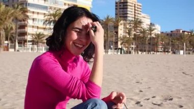 Genç bir kadın sahilde sigara içiyor ve gülümsüyor.