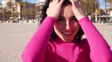 Sahilde gülümseyen genç bir kadın şehrin arka planında