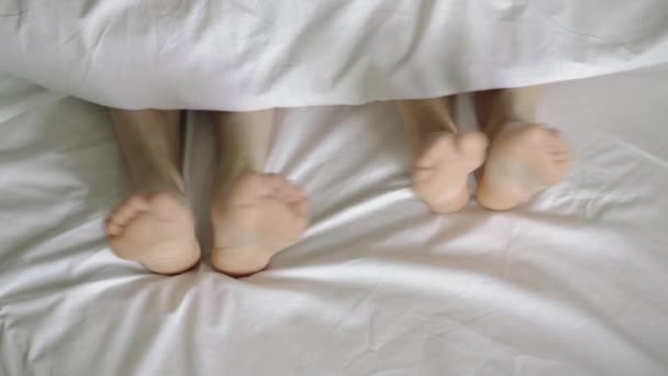 Et par stykker i sengen. Mand og kvinde ben top udsigt på en hvid seng. 4k – Stock-video