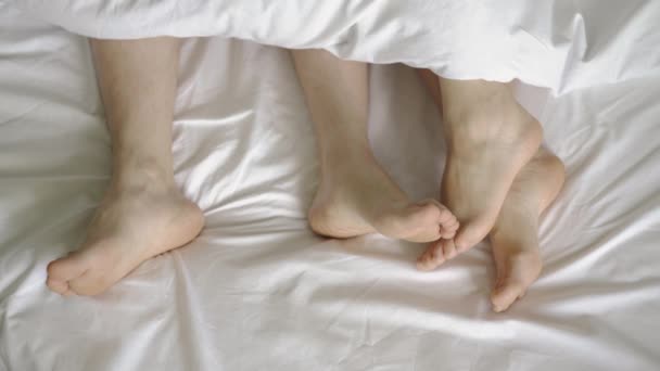 Пара в ліжку. Чоловічі та жіночі ноги зверху на білому ліжку. 4k — стокове відео