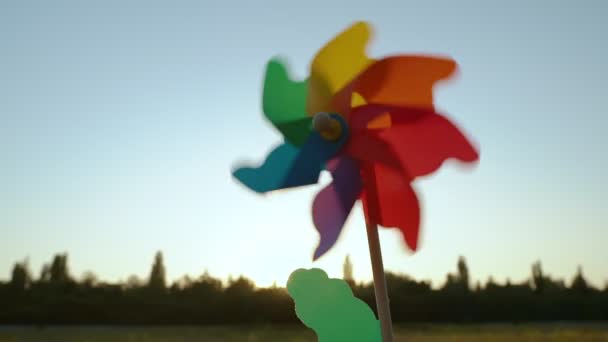Colorful paper windmill spinning in the blue sky against the skyline with trees — Stock videók