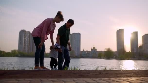 Young mother and father teach the child to walk along the path — Stockvideo