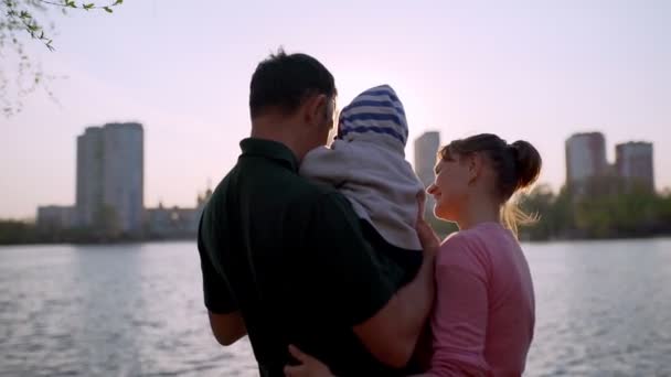 A happy family stands on the shore of the lake, admiring the sunset. — Stockvideo