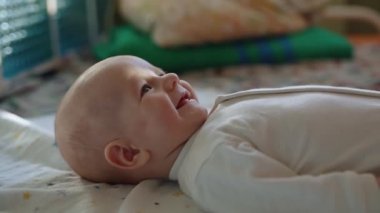 Sevimli bir bebek sırtüstü yatar, neşeyle gülümser ve kollarını sallar..