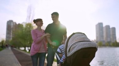 Genç bir aile göl kenarında bir bebek arabasıyla yürüyor.
