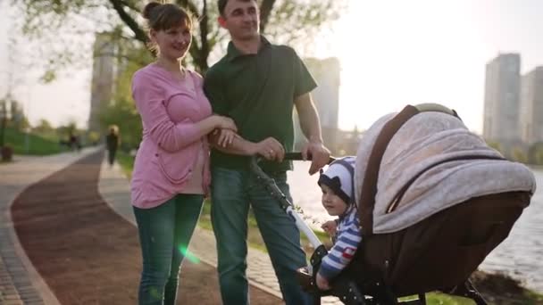 Young family walking with a pram near the lake — Stockvideo