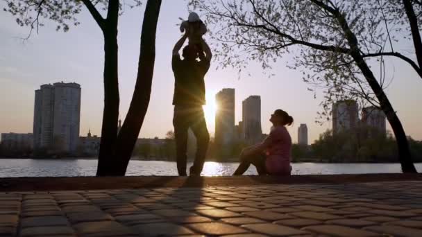 Dad holds the baby in his arms and circles, and mom admires. Family silhouette. — Stockvideo