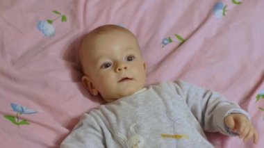 Sevimli bir bebek sırtüstü yatar, neşeyle gülümser ve kollarını sallar..