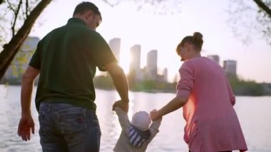 Gölün kenarında mutlu bir aile. Ebeveynler çocuğu iki eliyle tutar ve büyütür.