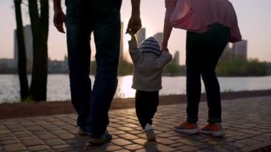 Young mother and father teach the child to walk along the path