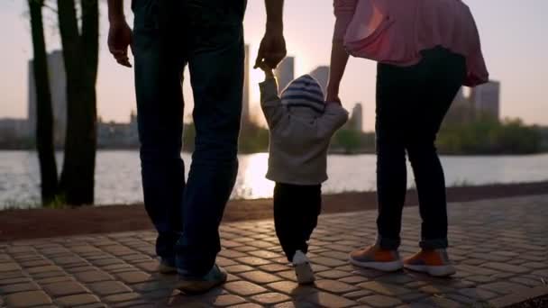 Young mother and father teach the child to walk along the path — Stockvideo