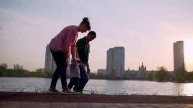 Genç anne ve baba çocuğa yol boyunca yürümeyi öğretir.