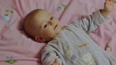 Sevimli bir bebek sırtüstü yatar, neşeyle gülümser ve kollarını sallar..