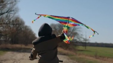 Gökkuşağı uçurtması olan mutlu bir çocuk bisiklet sürüyor..