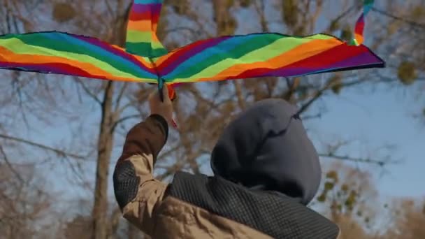 A happy boy with a flying rainbow kite rides a bicycle on the road. — Video Stock